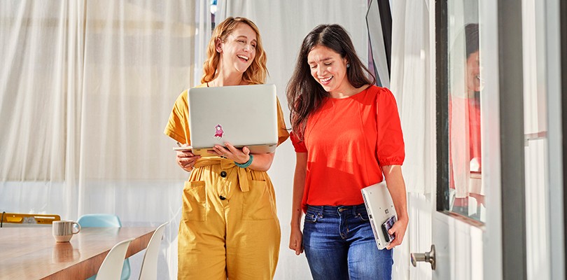 Two women walking with laptops