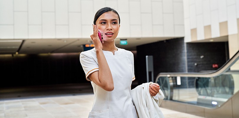 A woman standing outside talking on her phone while holding a jacket in her arm.