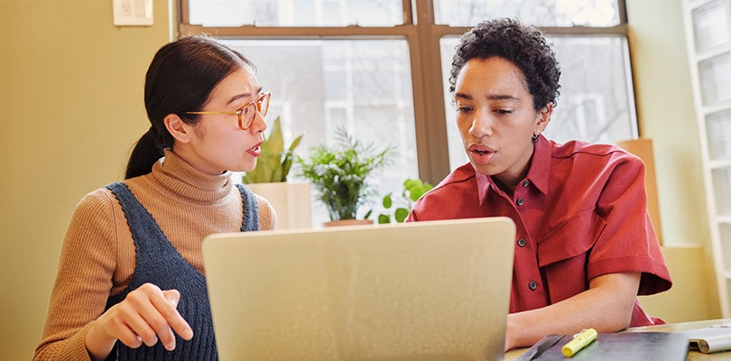 Two women collaborating in a meeting room at a laptop