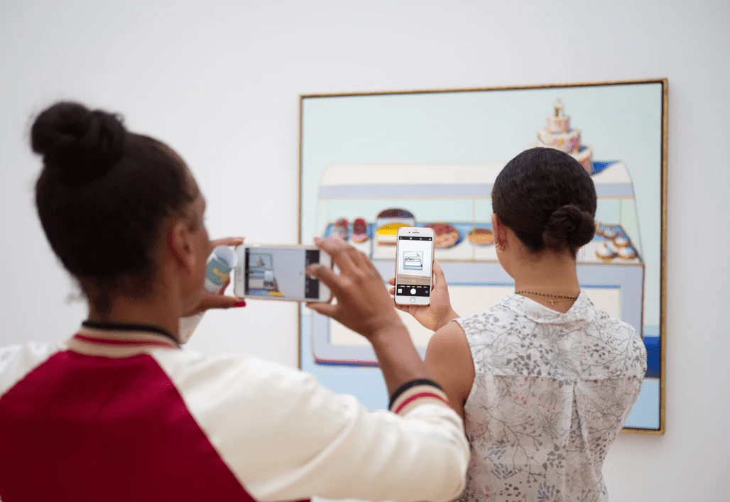 Two women taking photos of a piece of art in a gallery