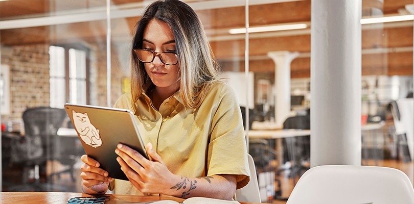 Woman sitting in conference room, looking down at a tablet she's holding that has cat sticker on the back.