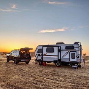 An RV is set up ready to camp in an open farm field, as the sun sets. Photo CC by mikepmiller