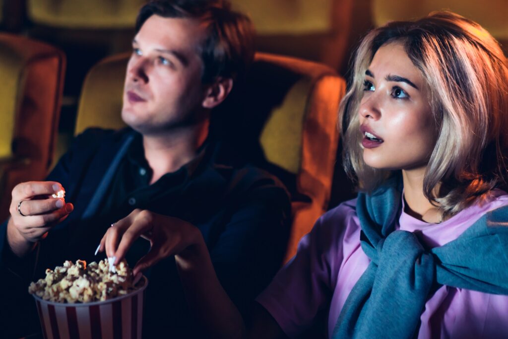 Couple eating popcorn and watching a movie at the theater.