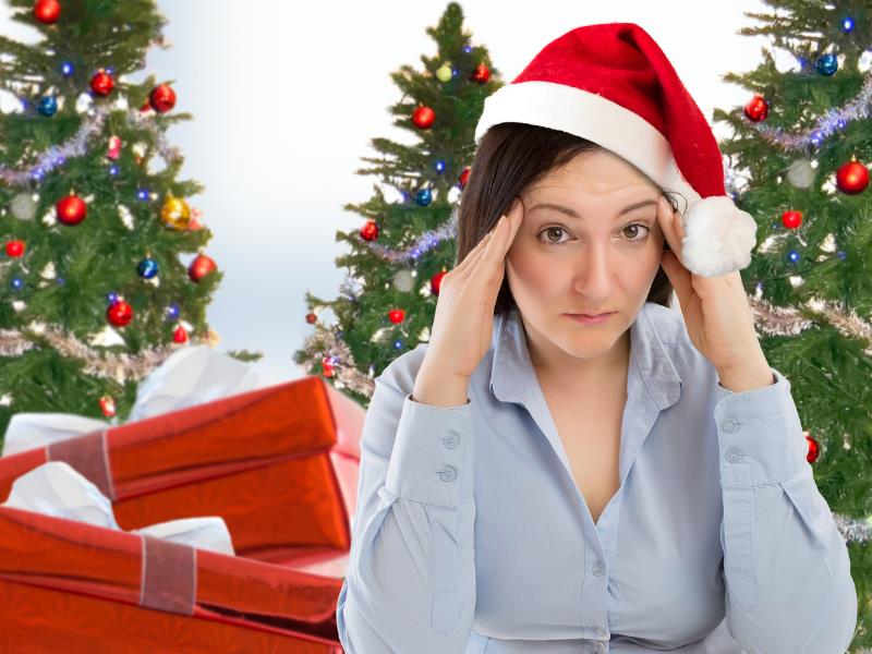 Woman among Christmas gifts showing holiday stress by massaging her temples