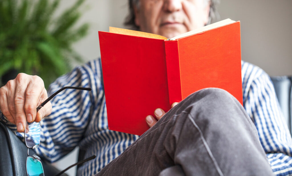 Older individual reading a book in a sunlit armchair